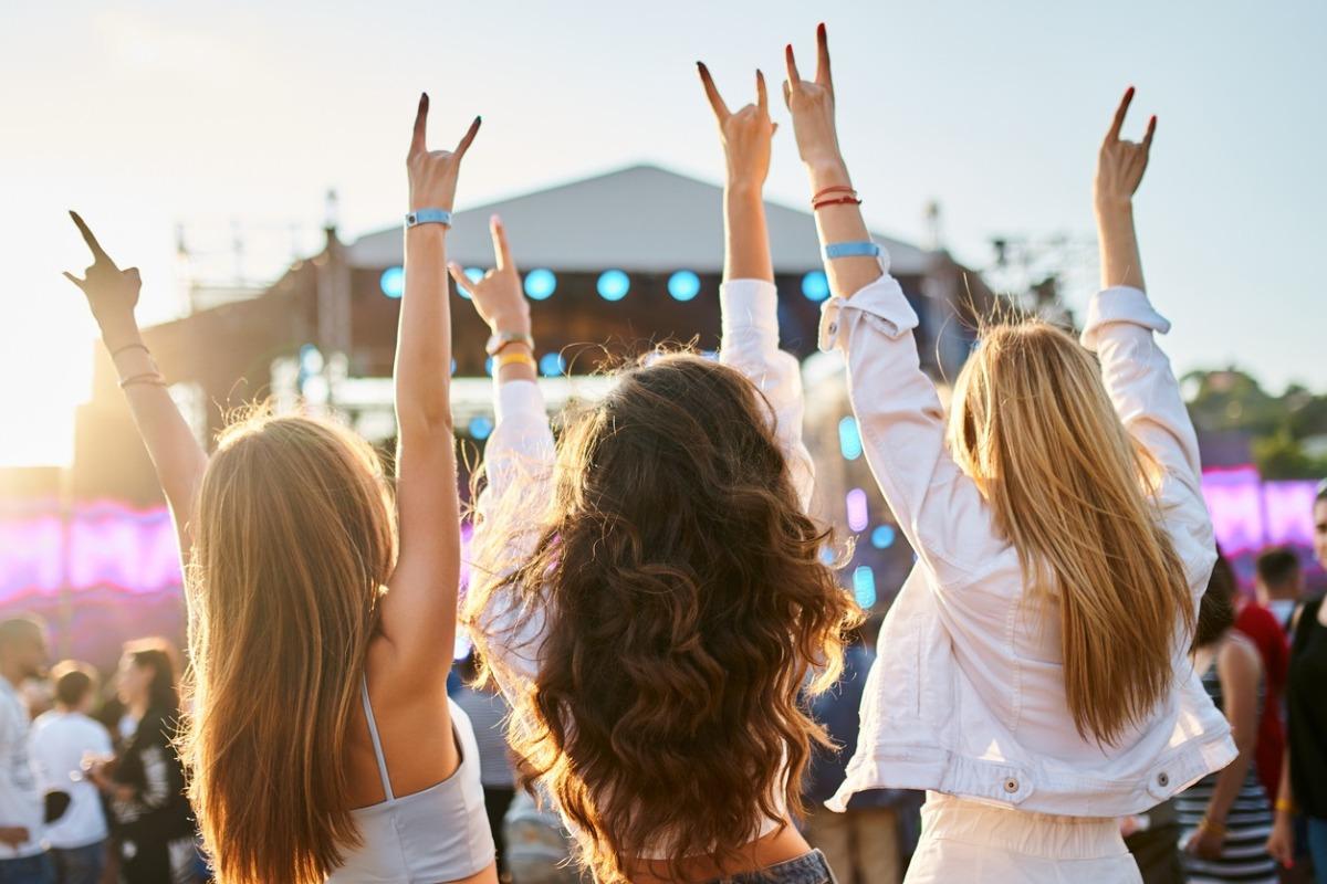 Group of female friends enjoying live music on sunny beach festival. Casual fun, youth culture, outdoor event by sea